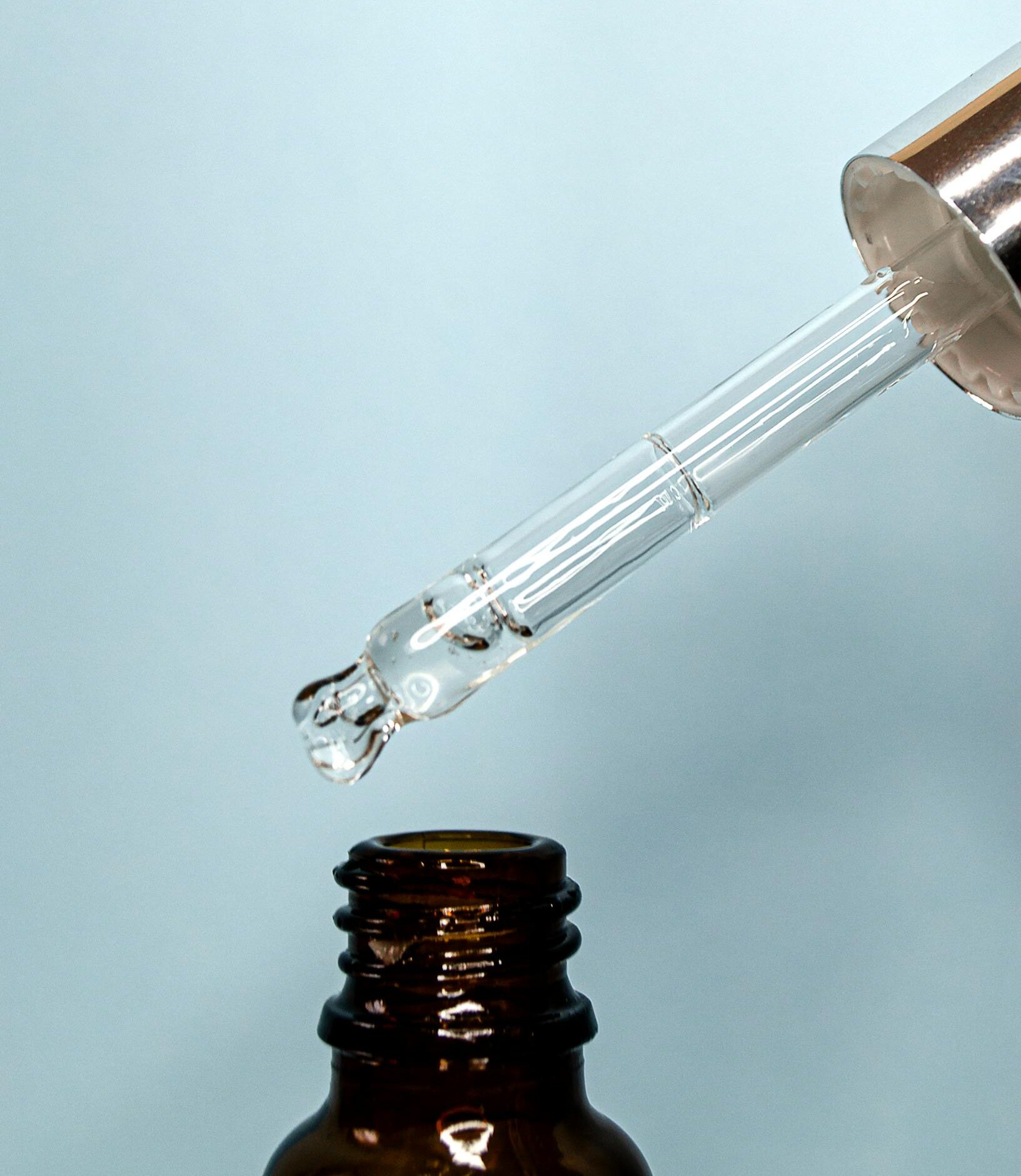 A transparent dropper releasing liquid into an empty brown glass bottle.