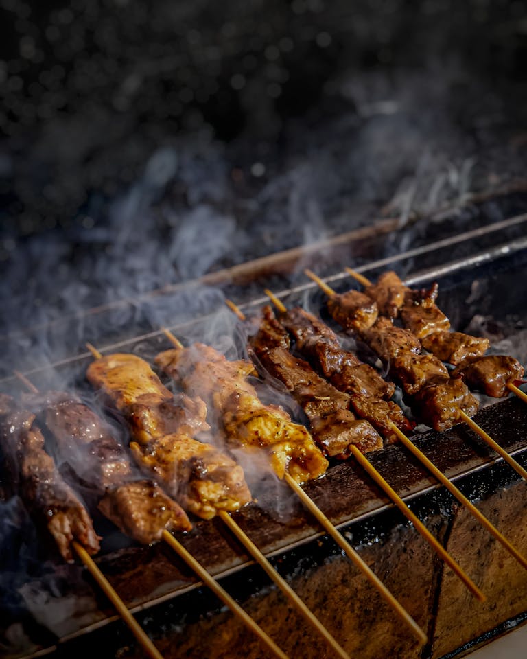 Delicious beef and chicken skewers grilling on a smoky charcoal barbecue in Subang, Indonesia.