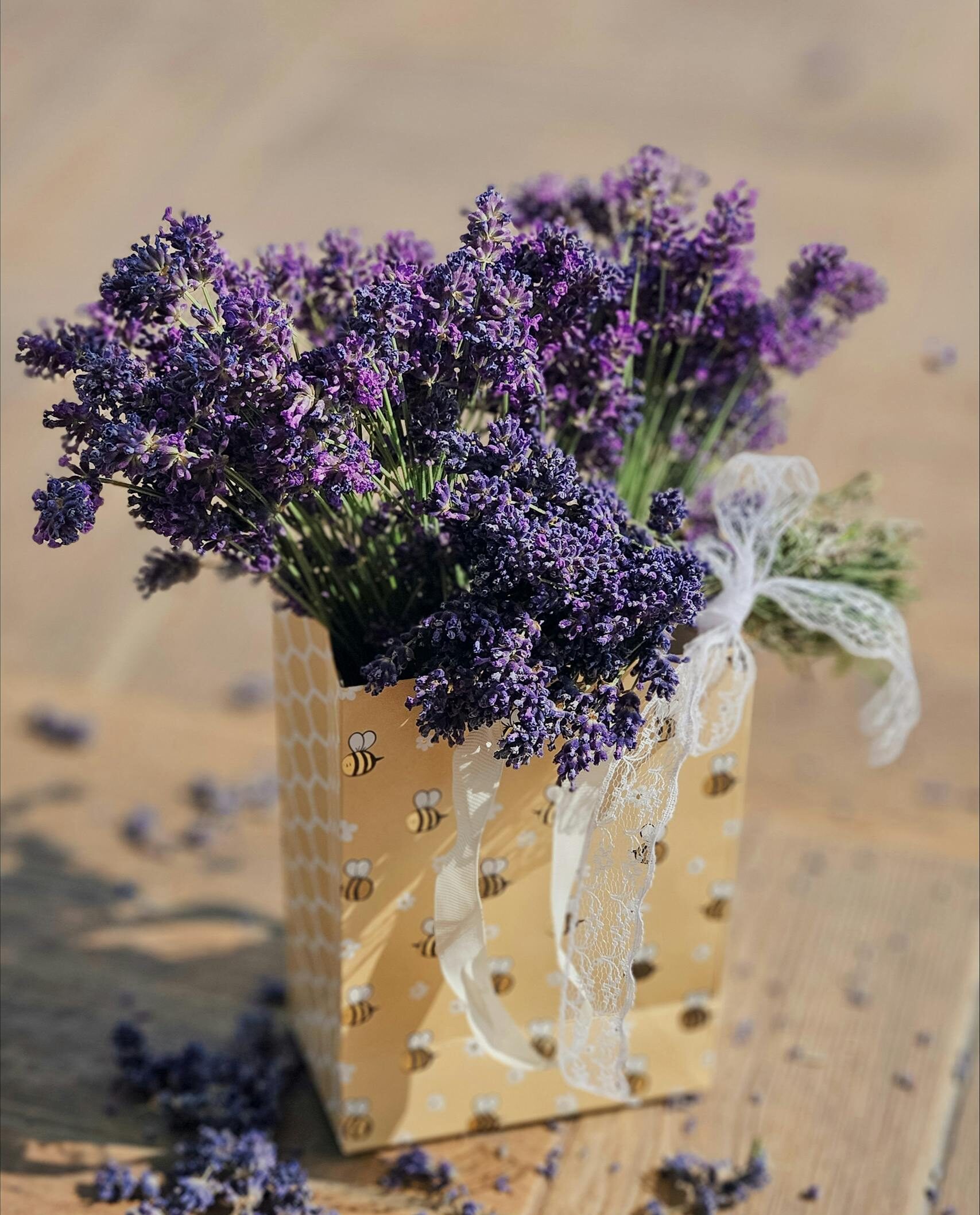 Rustic lavender bouquet in bee-patterned bag on wooden table, perfect for home decor.